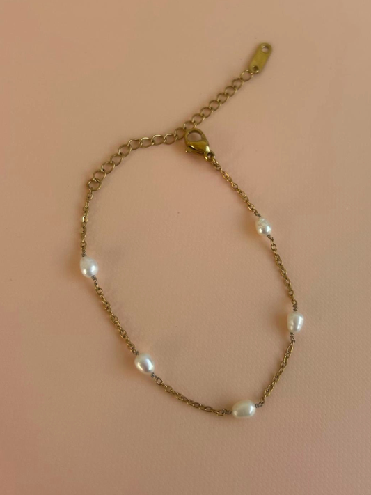 A delicate gold chain bracelet with five small white baroque pearls spaced along the chain, featuring a lobster clasp and extender chain, displayed on a solid pink background. By Nicola and Coco & Lola Exclusive