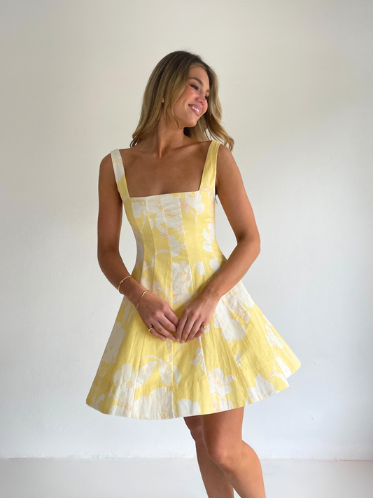 By Nicola Milly mini dress in amarilla flor yellow floral print in cotton linen with  straps and flowy hem, perfect for daytime events and summer occasions. Exclusive to Coco & Lola